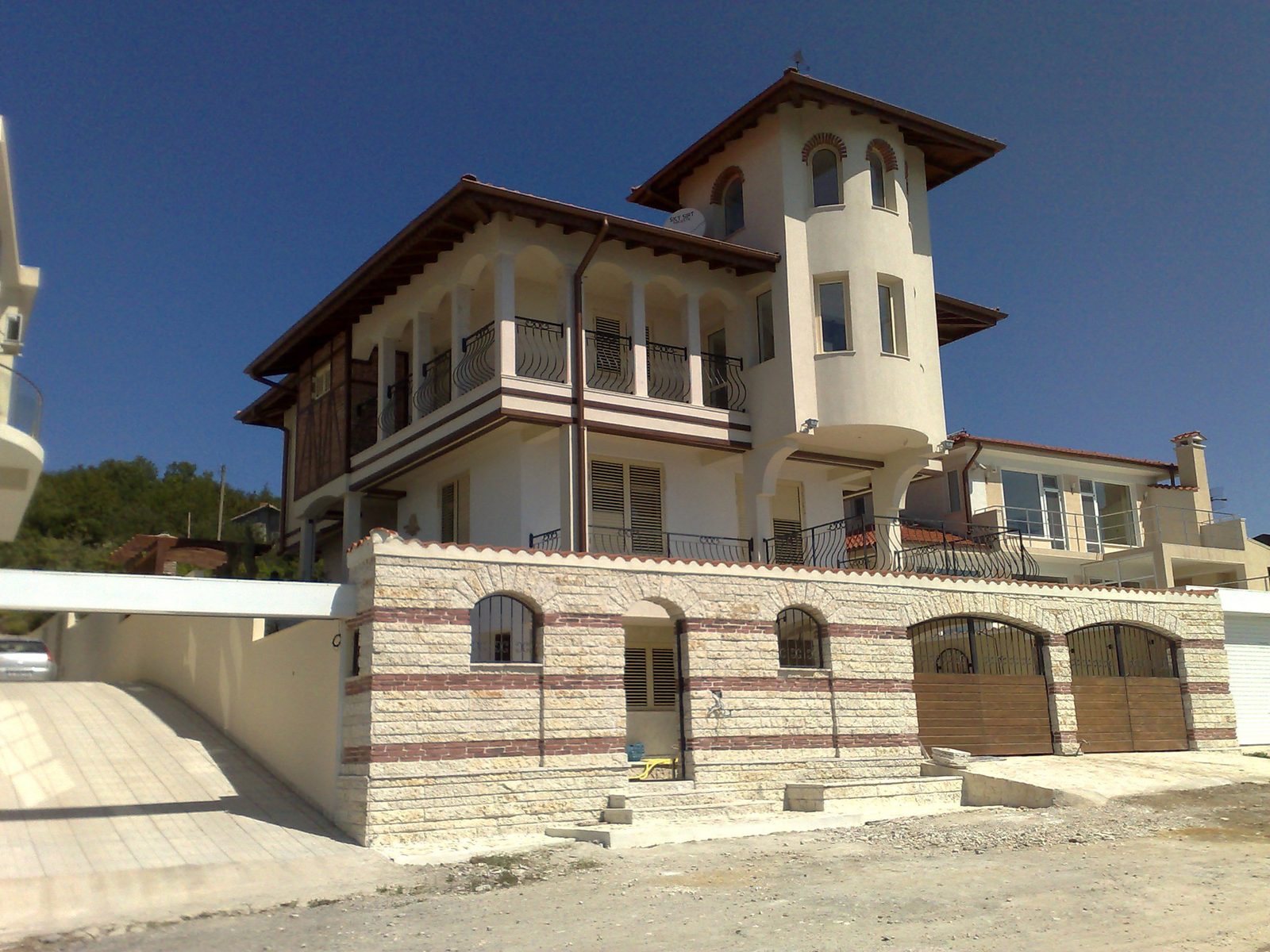 Casa terminată, văzută de pe drum: turnul rotund, loggiile cu balustradă de fier forjat și soclul de piatră